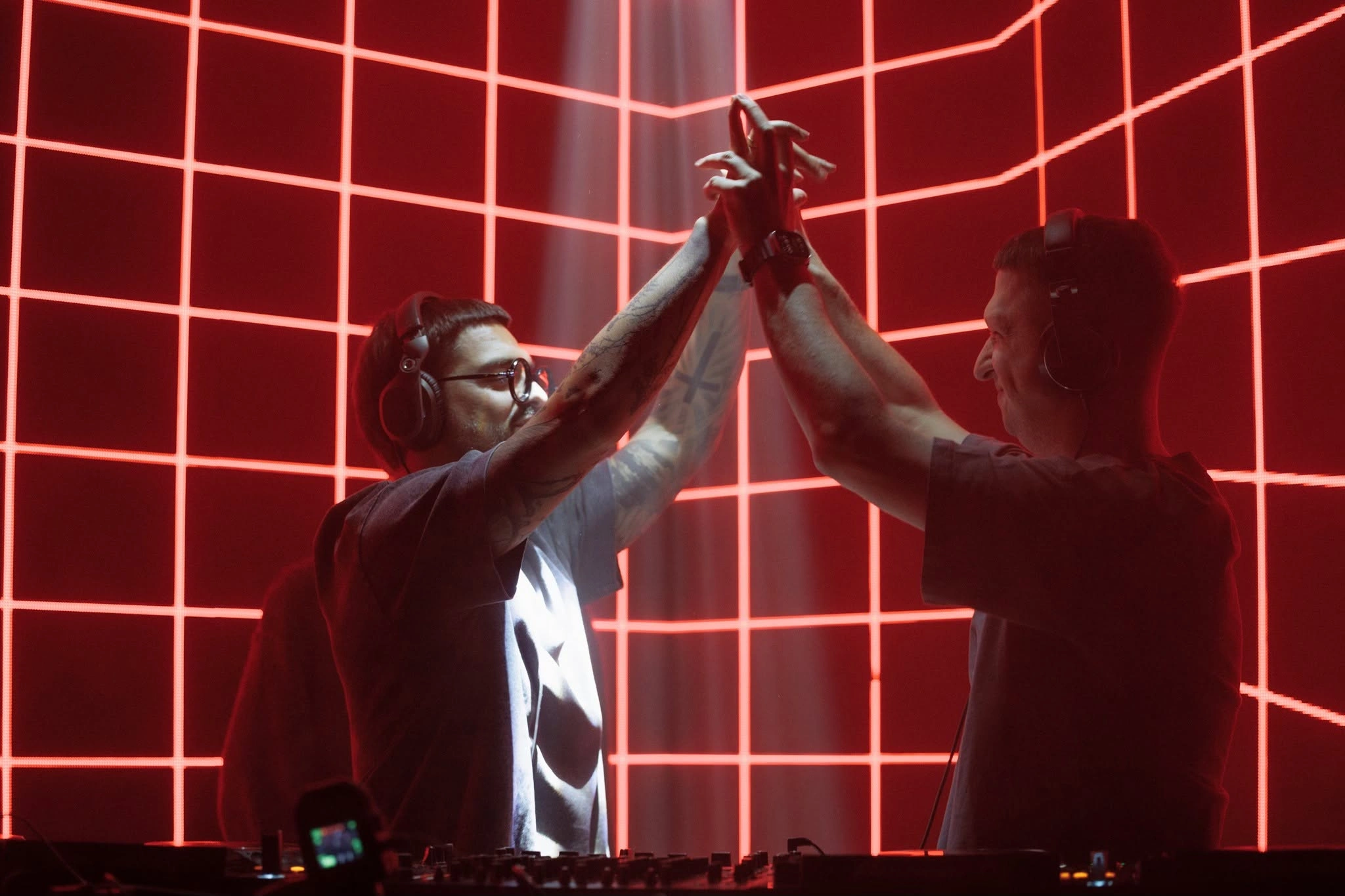 DJs sharing a high five in front of a red light grid